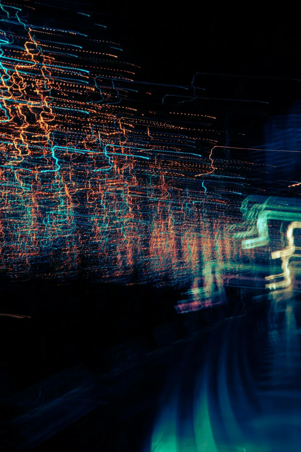 Long exposure light trails in vibrant orange and teal against a dark background
